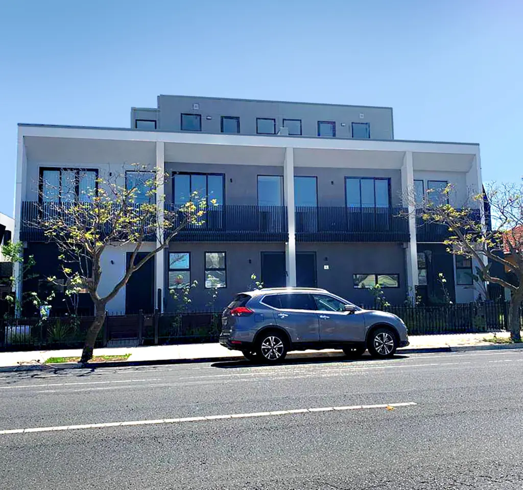 Modern residential apartment building with completed exterior facade and parked cars in front.