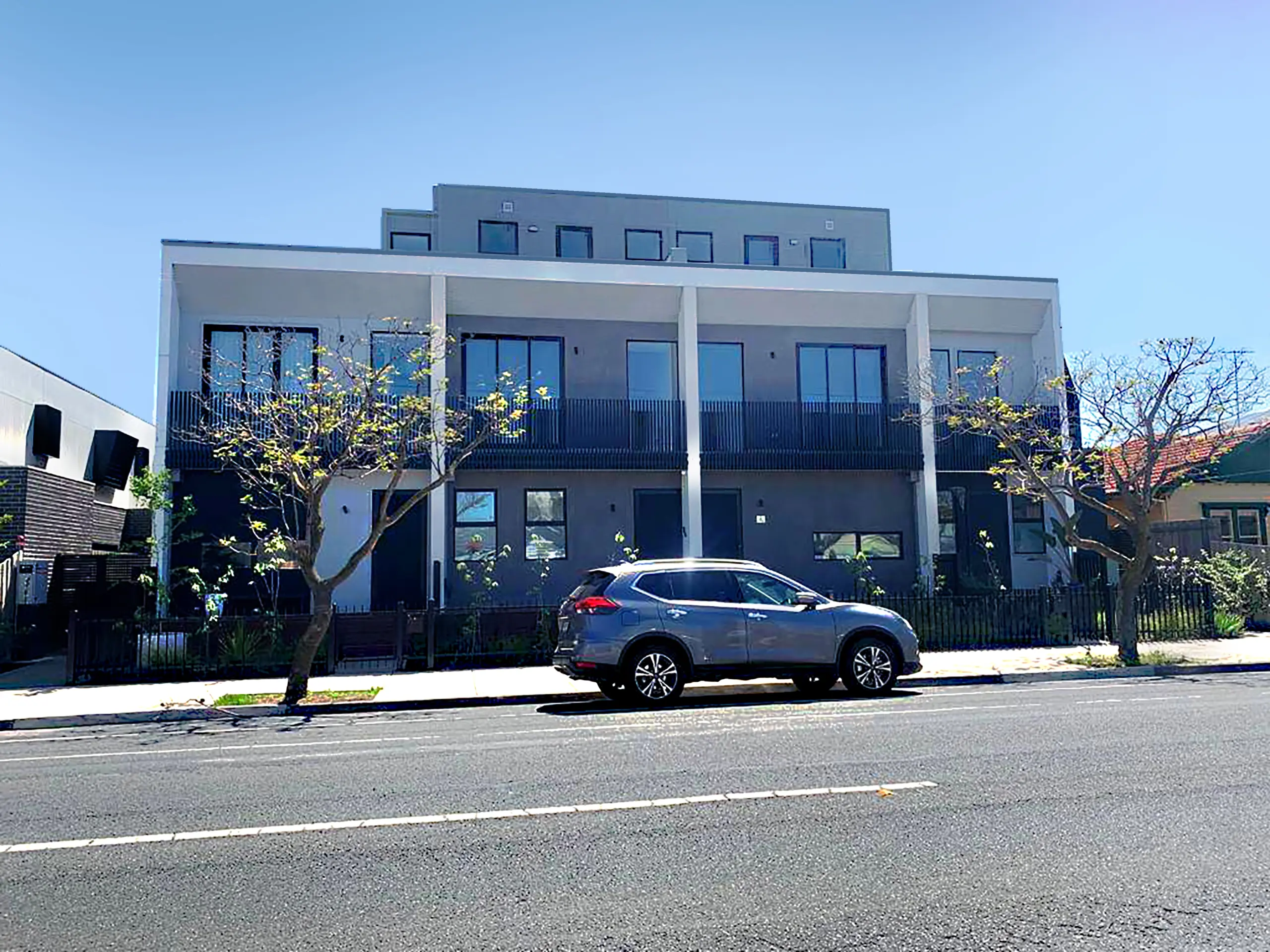 A modern townhouse building with clean lines, large windows, and a car parked in front