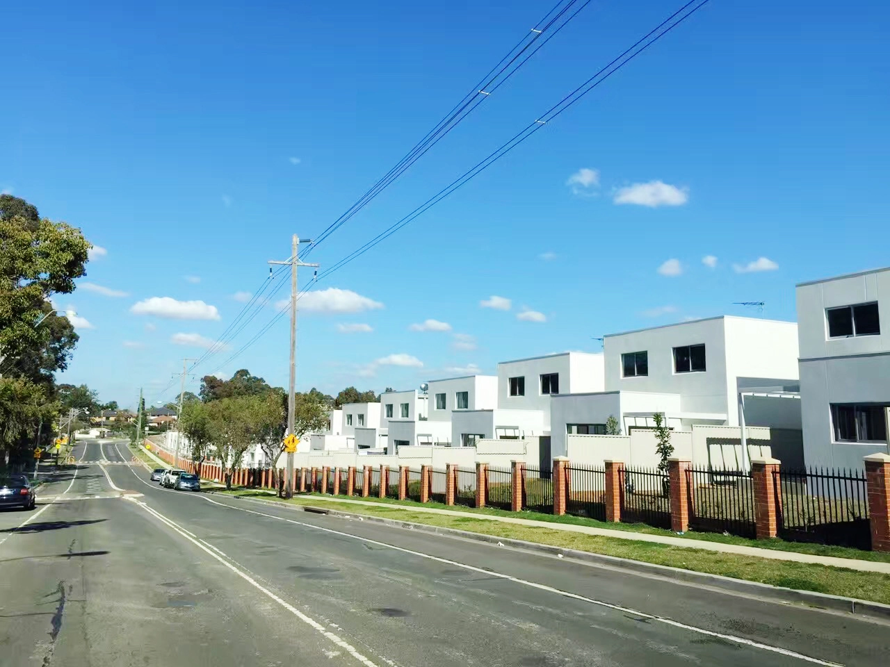 A row of modern white two level homes along a wide street under a clear blue sky